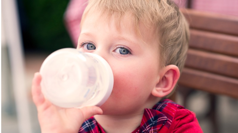 Un très jeune enfant tient un biberon rempli de lait de croissance 